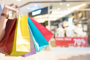 Die Hand einer Frau hält mehrere bunte Einkaufstüten aus Papier.