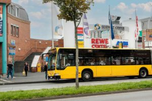 Vor dem Haupteingang des Seidnitz Centers hält ein gelber Linienbus. Im Hintergrund sind die bunten Flaggen vor dem Center zu sehen.